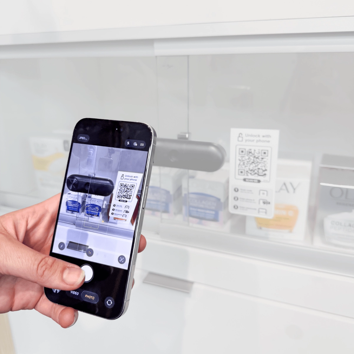 한 쇼핑객이 휴대폰으로 ‘Customer Self-Access’ QR 코드를 스캔하여, ‘ InVue  ’의 ‘LIVE ’ 슬라이더 잠금장치로 잠겨 있는 미용용 유리 슬라이딩 케이스의 잠금을 해제하고 있다.